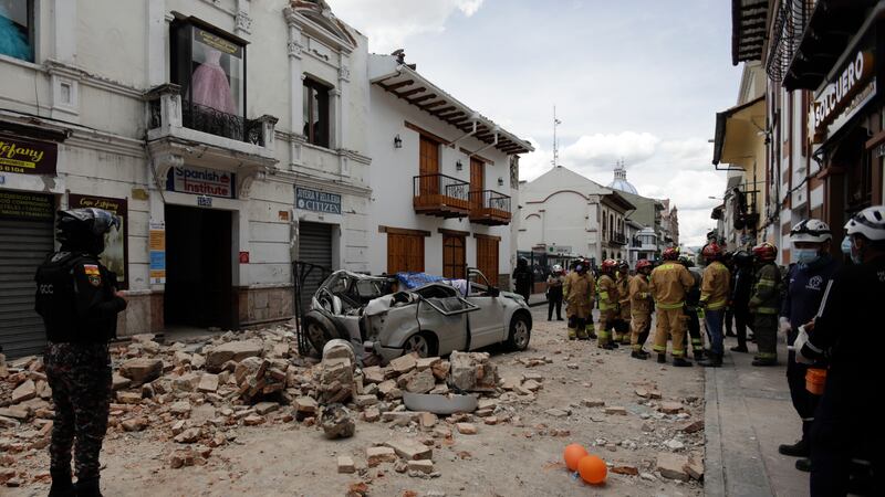 Rescue workers stand next to a car crushed by debris after an earthquake in Cuenca, Ecuador,...